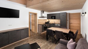 A modern kitchen with wooden cabinets, a dining area with a wooden table and chairs, and a TV mounted on the wall.