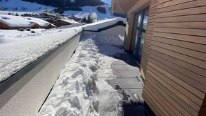 A snow-covered outdoor area with a wooden building, a metal staircase, and a mountain in the background.