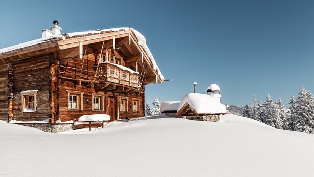 A wooden cabin with a balcony, surrounded by snow-covered trees.
