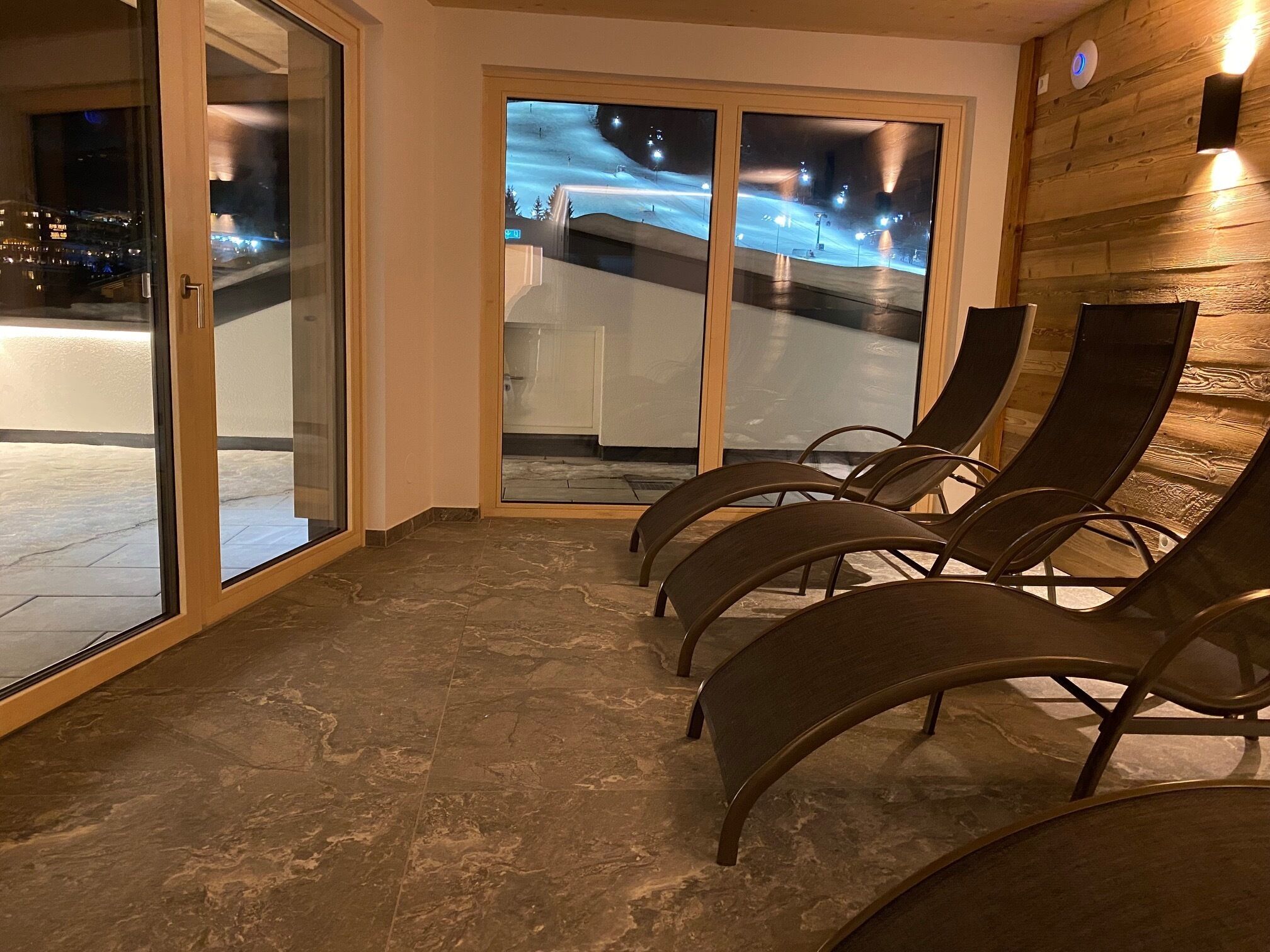 Un espace d’attente avec vue sur une piste de ski illuminée la nuit.