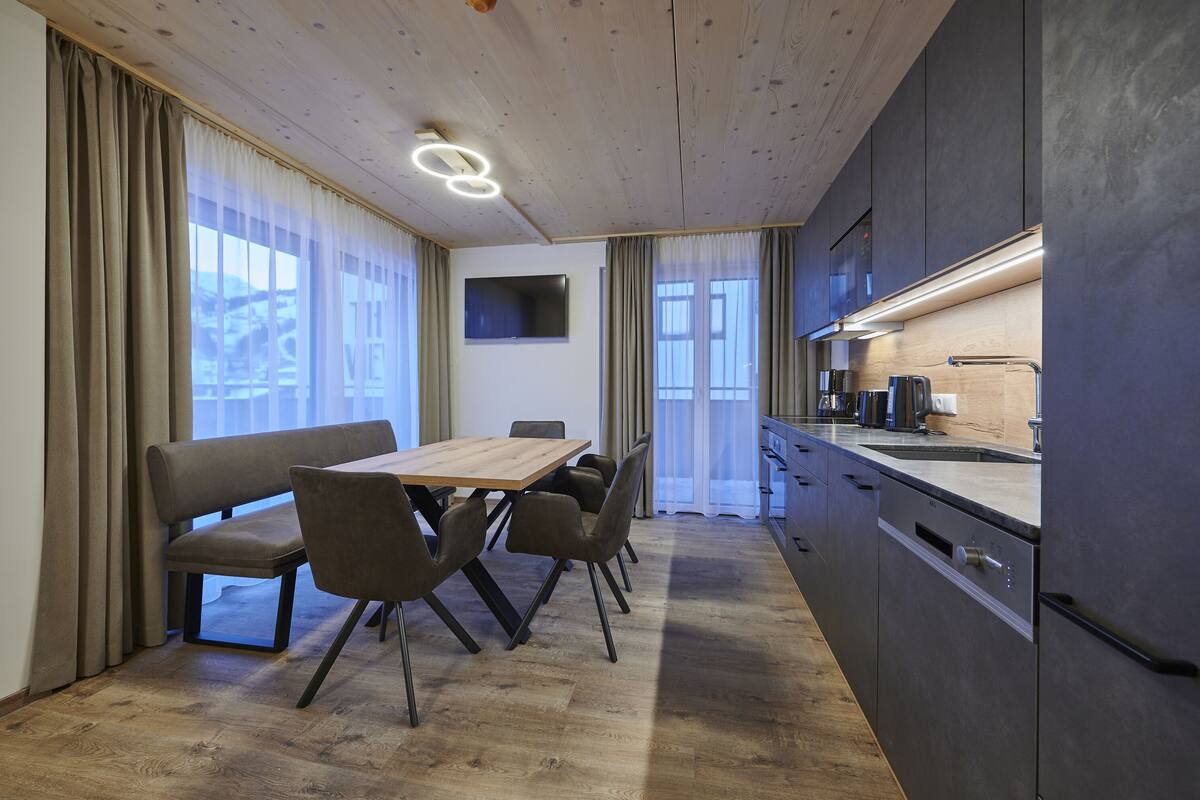 Una cocina moderna con una mesa y sillas de madera, horno empotrado y un televisor de pantalla plana en la pared.