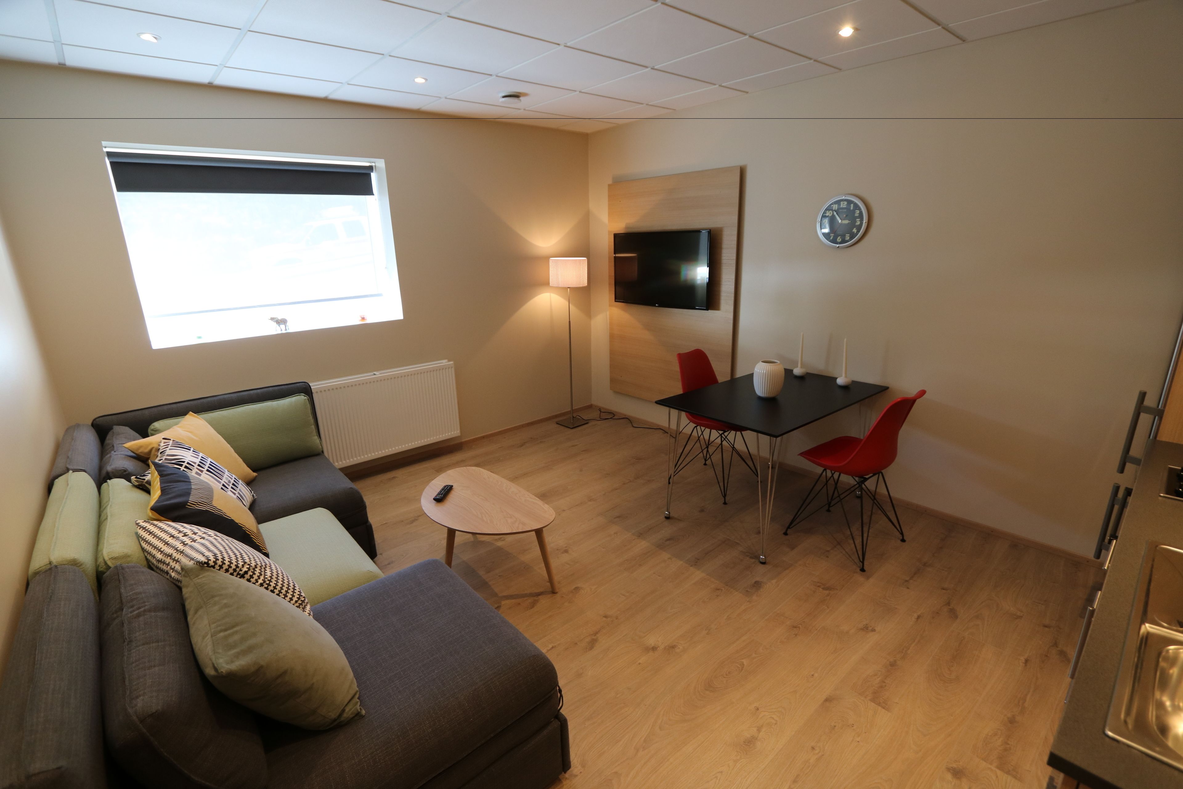 Un salon moderne comprenant un canapé, une petite table, une table à manger avec des chaises, un téléviseur et une horloge murale.