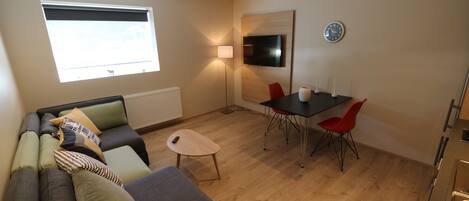 Un salon moderne comprenant un canapé, une petite table, une table à manger avec des chaises, un téléviseur et une horloge murale.