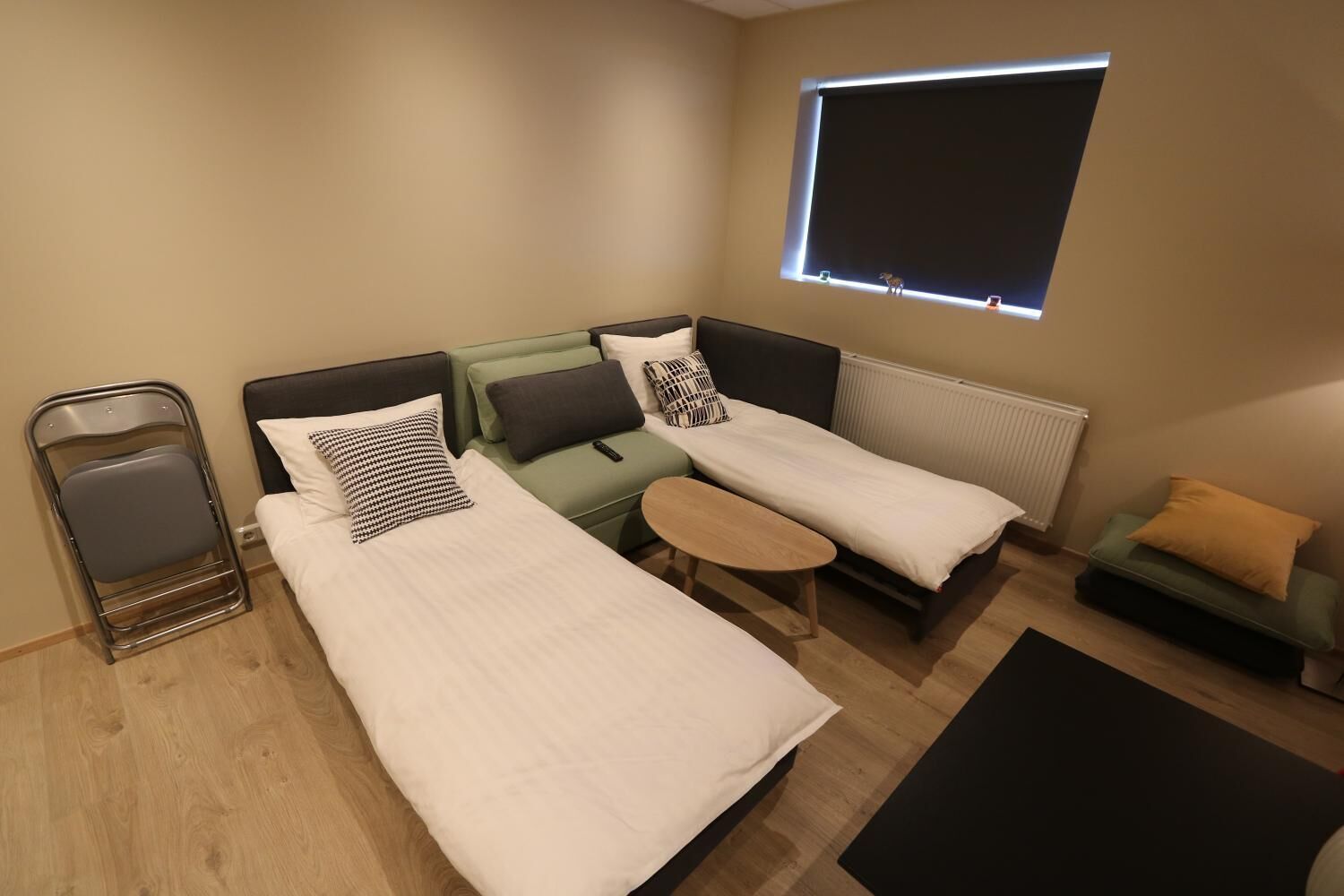 Habitación pequeña con dos camas individuales, una mesita, una silla y una ventana con persianas.