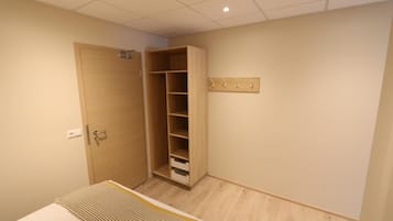 Un dormitorio con un armario de madera, una cama con manta a rayas y una lámpara de pared.