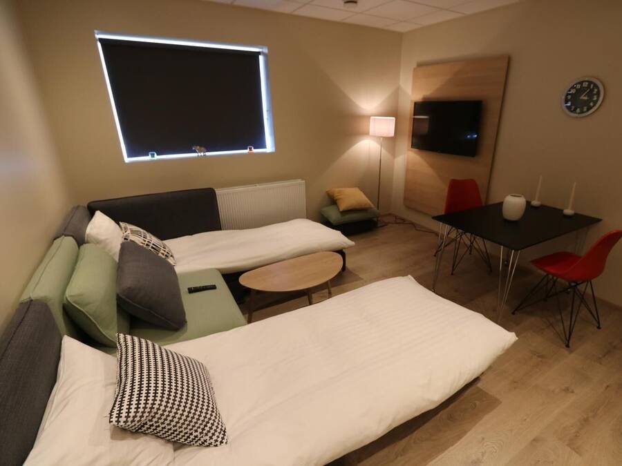 Una habitación de hotel compacta con dos camas individuales, un sofá, una mesita, un televisor y una zona de comedor con una mesa y sillas.