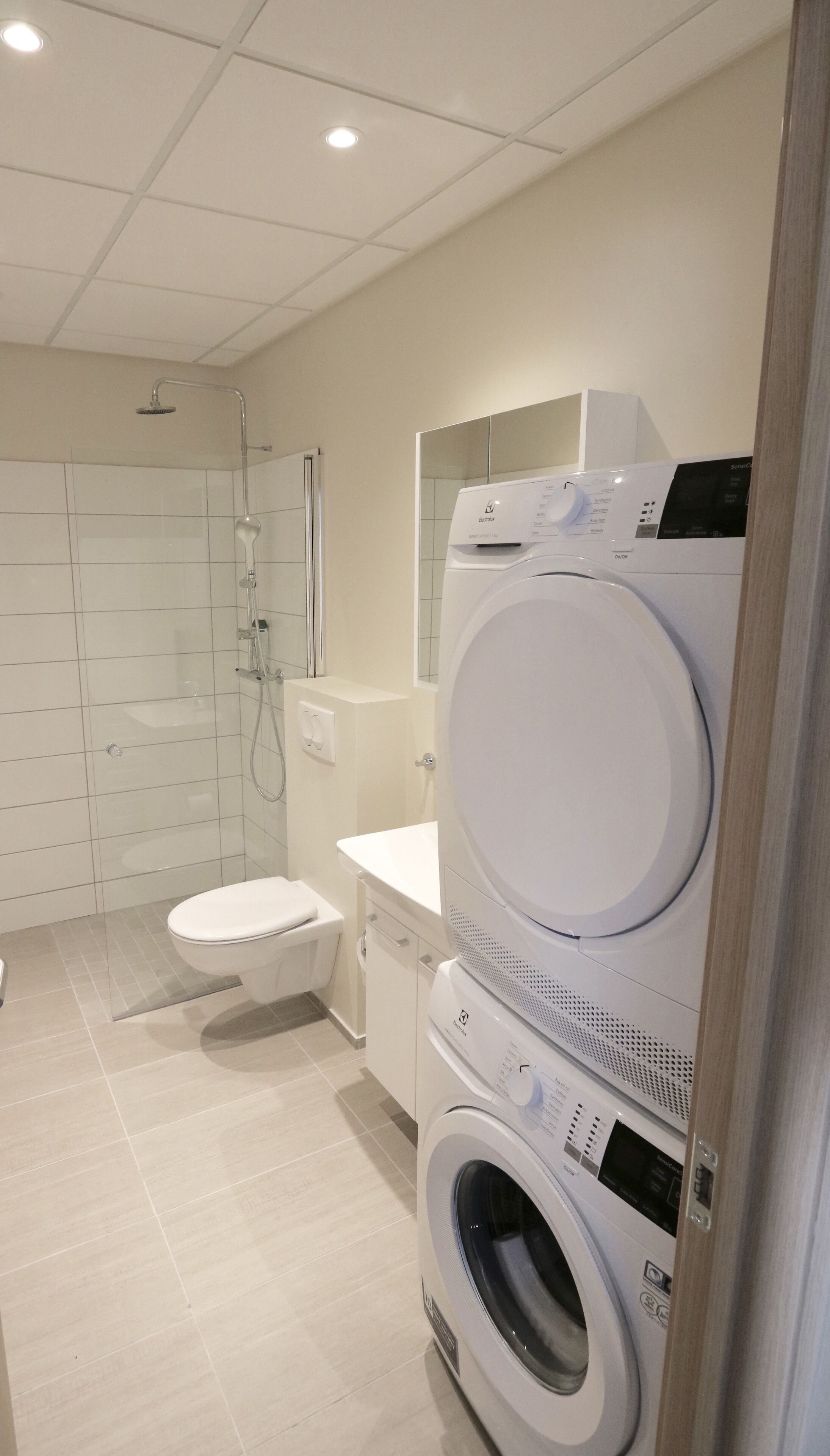 A modern bathroom with a toilet, a washing machine, and a shower.