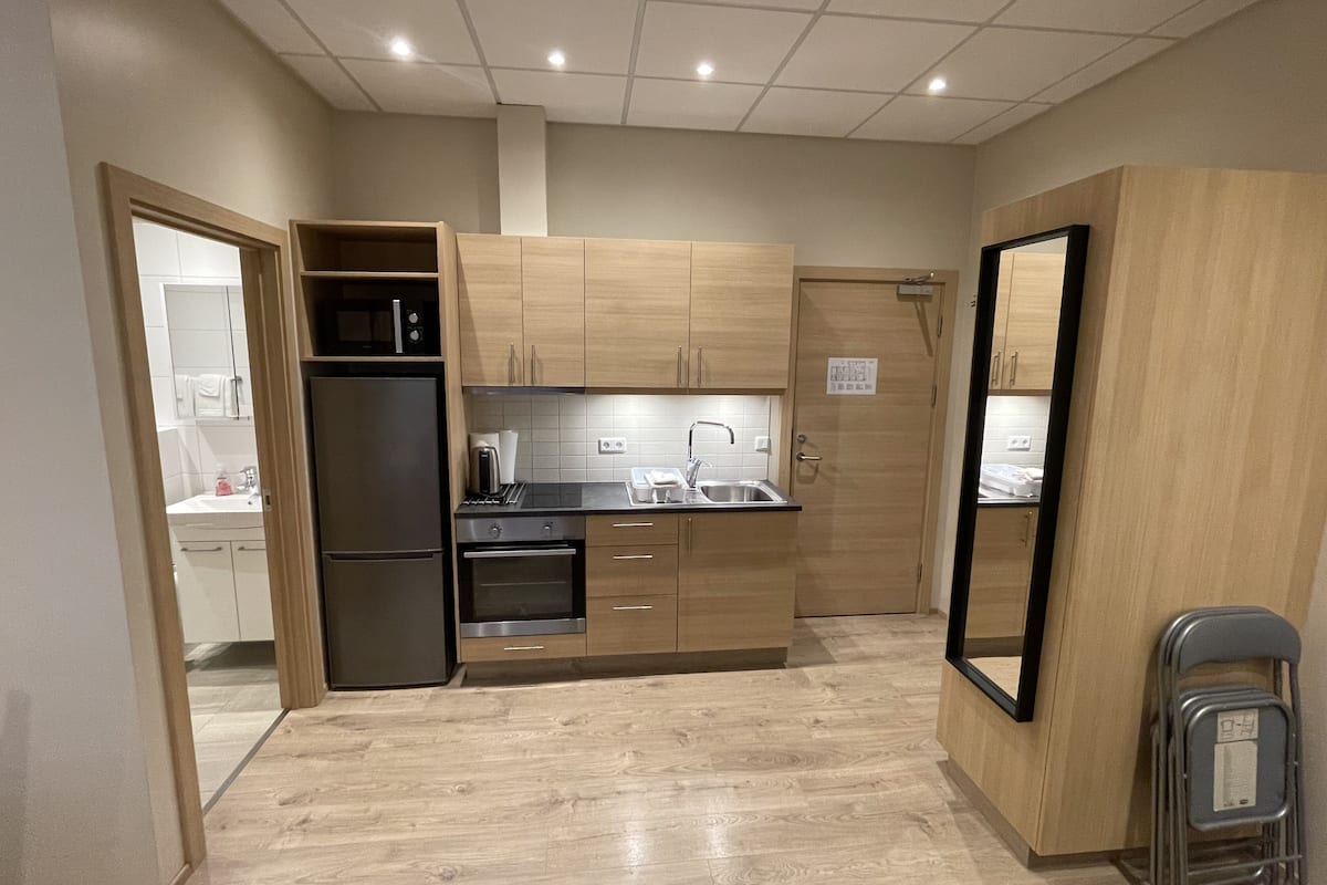 A compact kitchen with wooden cabinets, a stainless steel refrigerator, a built-in oven, and a sink.
