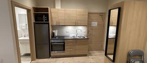 A compact kitchen with wooden cabinets, a stainless steel refrigerator, a built-in oven, and a sink.
