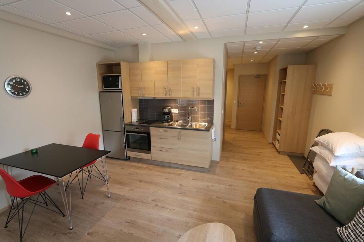 A compact living space with a kitchenette, a dining area with a table and chairs, and a sofa with pillows.