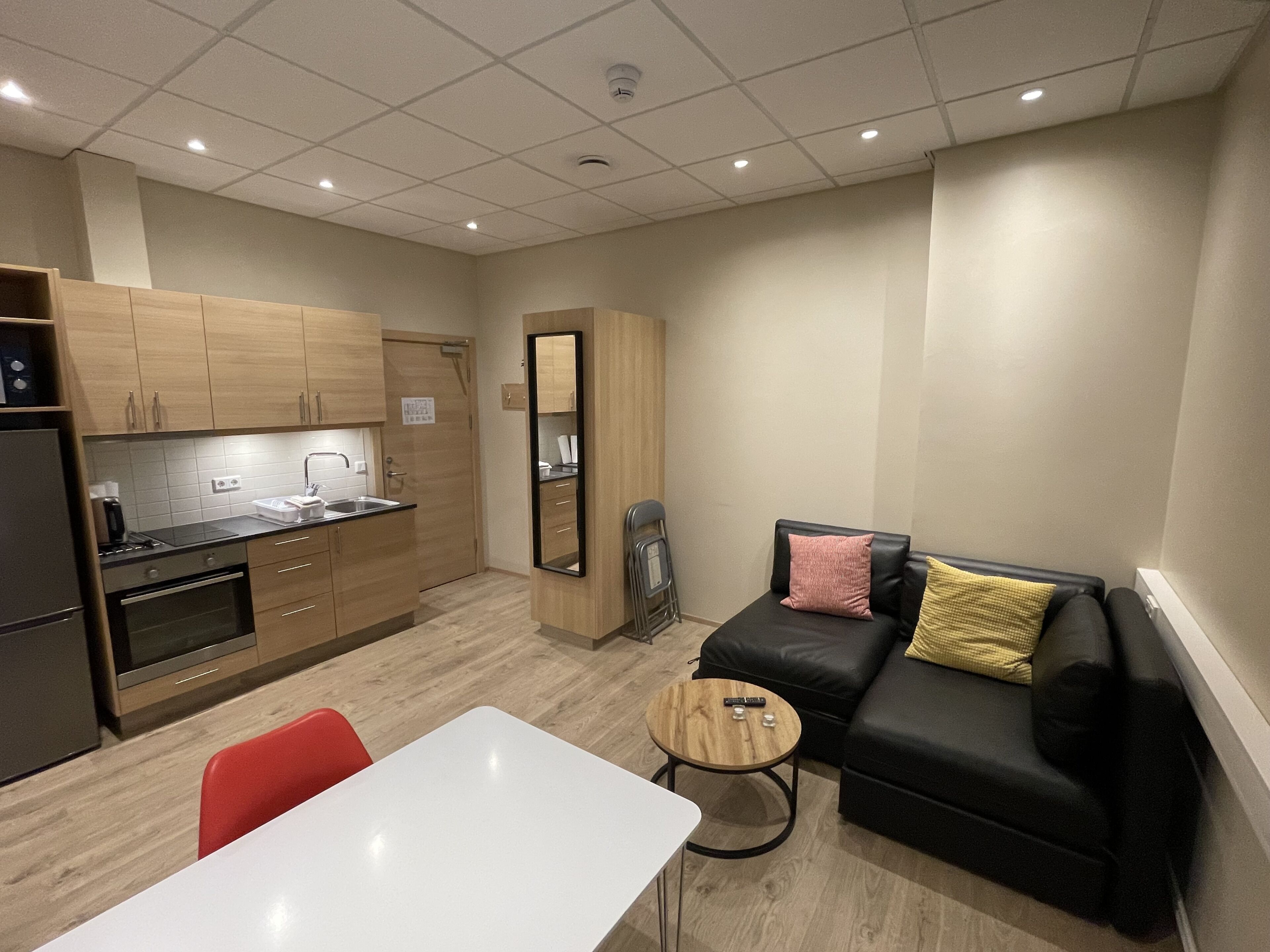 Een knus woongedeelte met een kitchenette, een bank, een tafeltje en een spiegel.