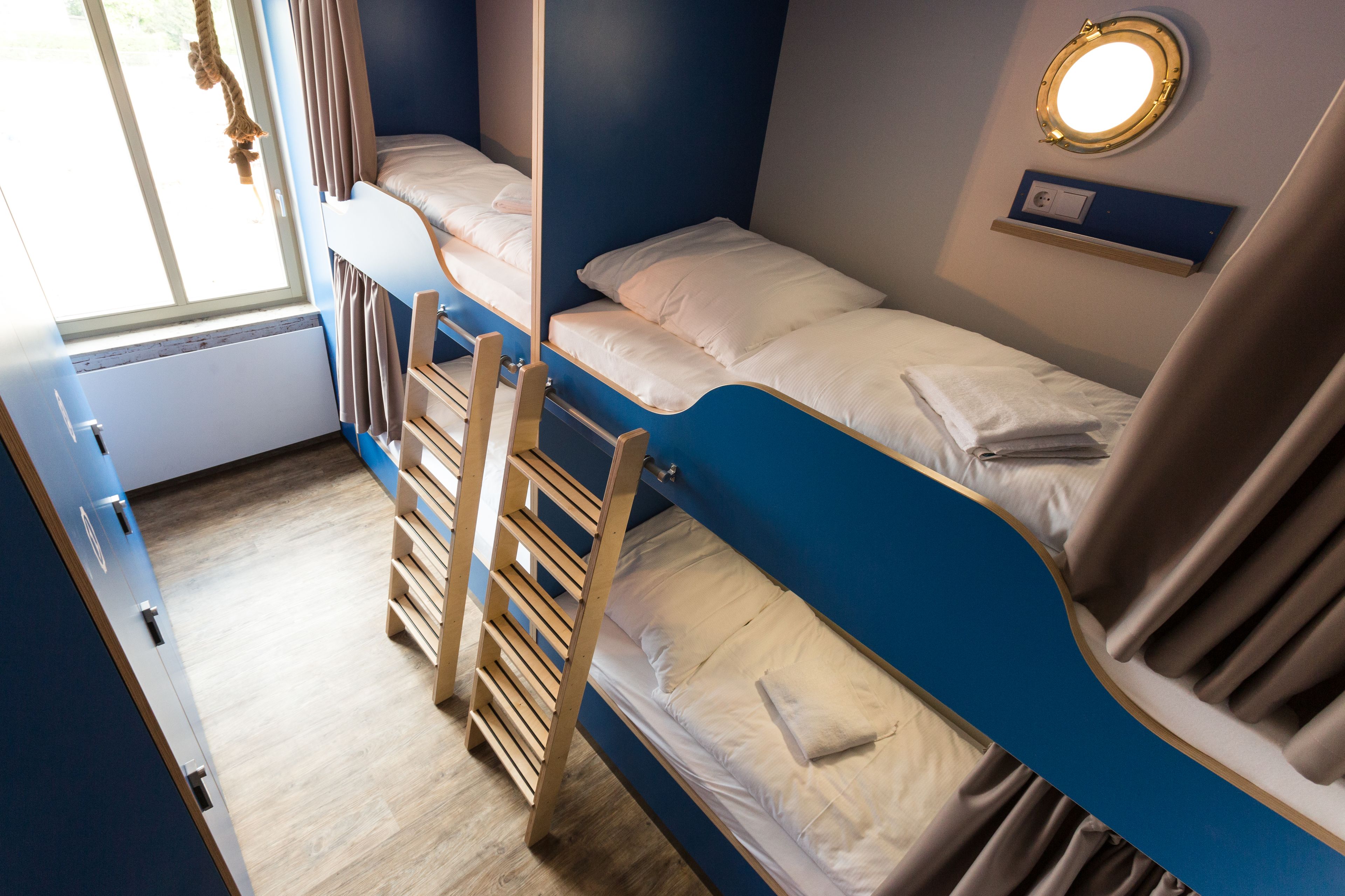 Ein Schlafzimmer mit Etagenbetten, einer Leiter, einem Fenster mit Vorhängen und einem Spiegel an der Wand.