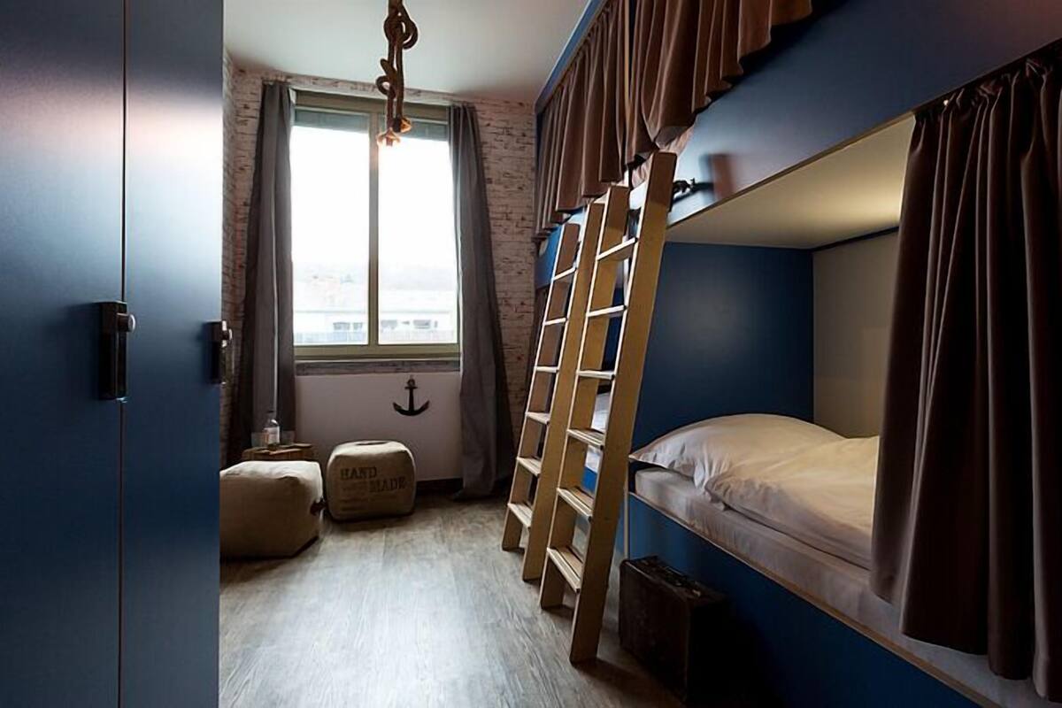 A bunk bed room with a window, a hanging light fixture, and a small stool.