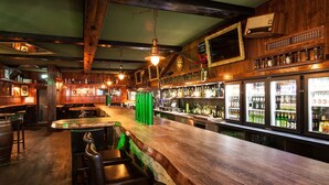Un bar avec des poutres en bois, des tabourets verts et un comptoir où sont exposées des bouteilles.