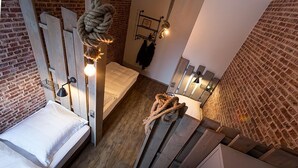 Une chambre de style loft avec un lit en mezzanine, une balançoire en corde et un mur en briques.