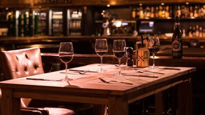Un bar avec une table en bois, quatre verres à vin et une bouteille de vin.