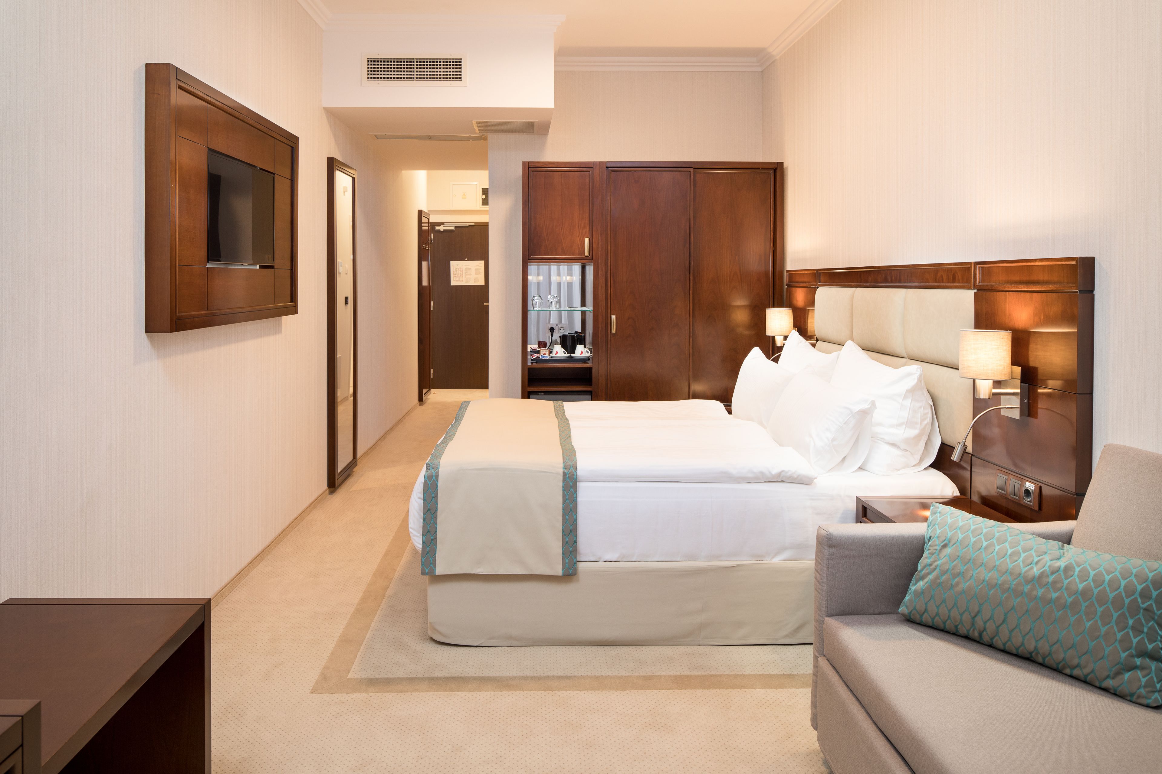 A hotel room with a double bed, a sofa, a TV, a wardrobe, and a desk.