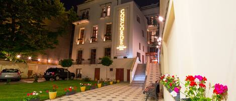 Un hotel con un patio empedrado, una escalera que conduce a la entrada y macetas con flores a lo largo del camino.