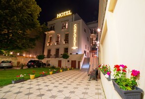 A hotel with a tiled courtyard, a staircase leading to the entrance, and flower planters along the pathway.