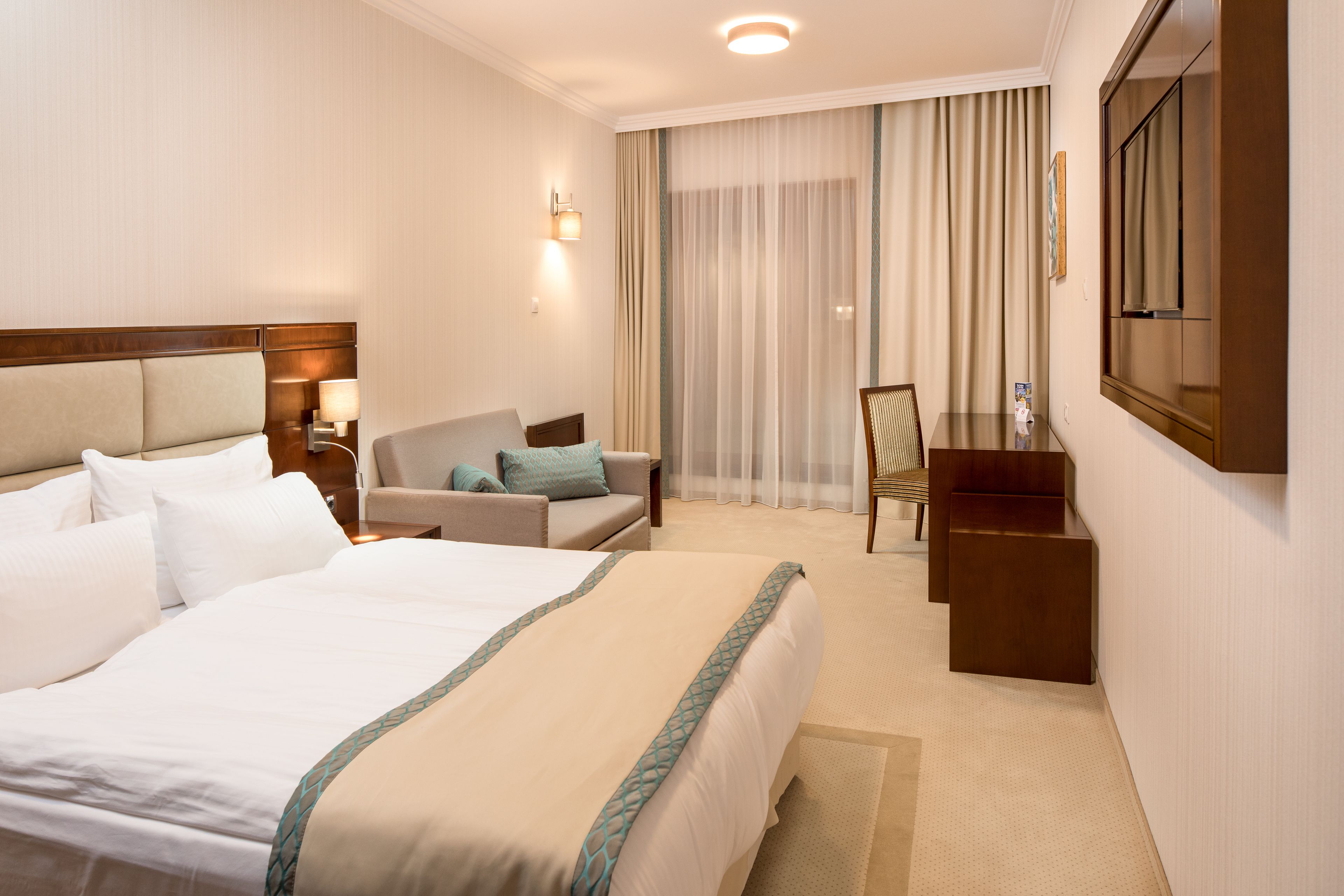 A hotel room with a large bed, a sofa, a desk, and a mirror.