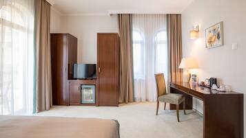Habitación de hotel con cama, escritorio con silla, televisión, minibar y ventana con cortinas.