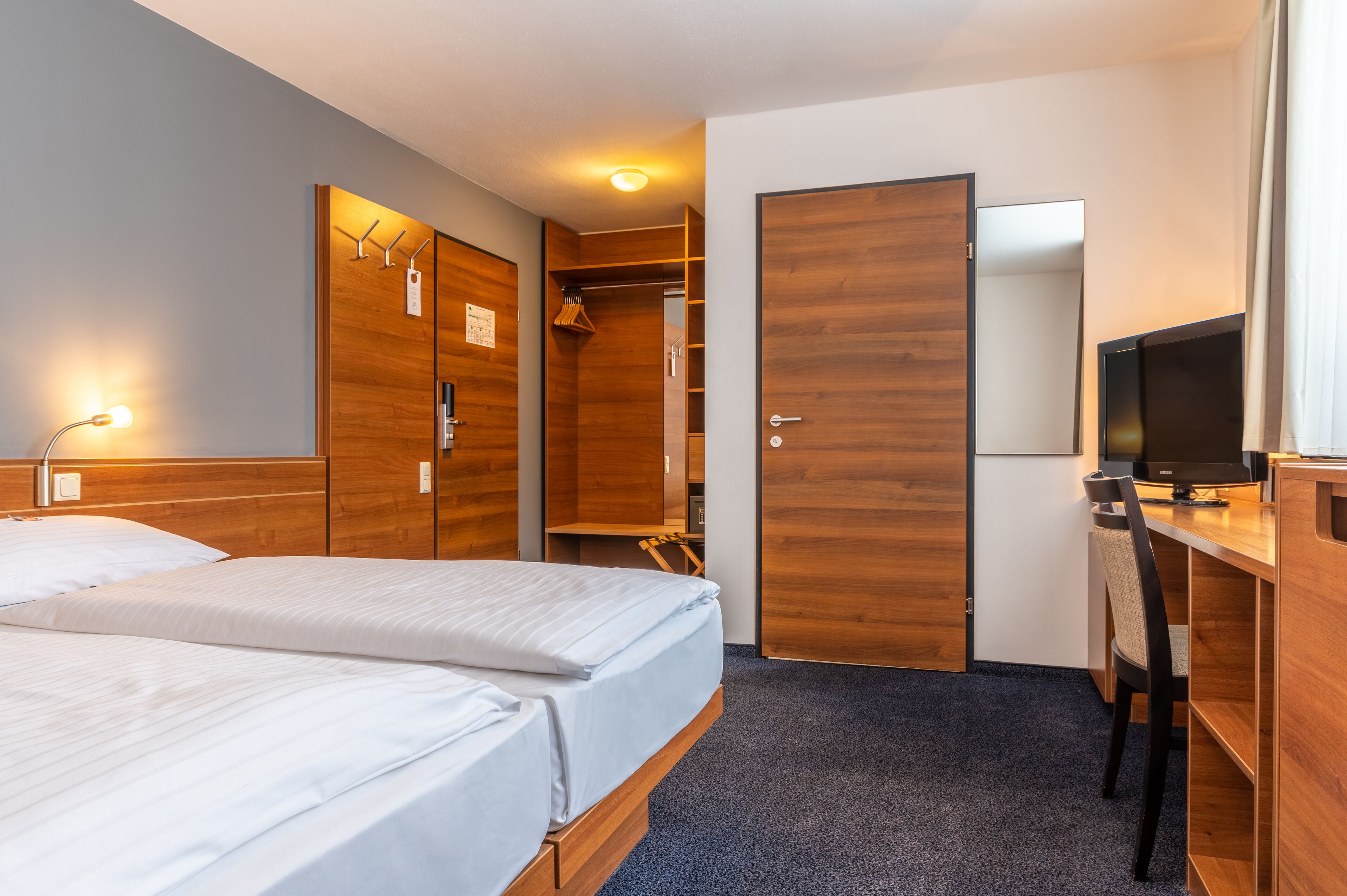 A hotel room with two beds, a desk with a chair, a wardrobe, and a television.