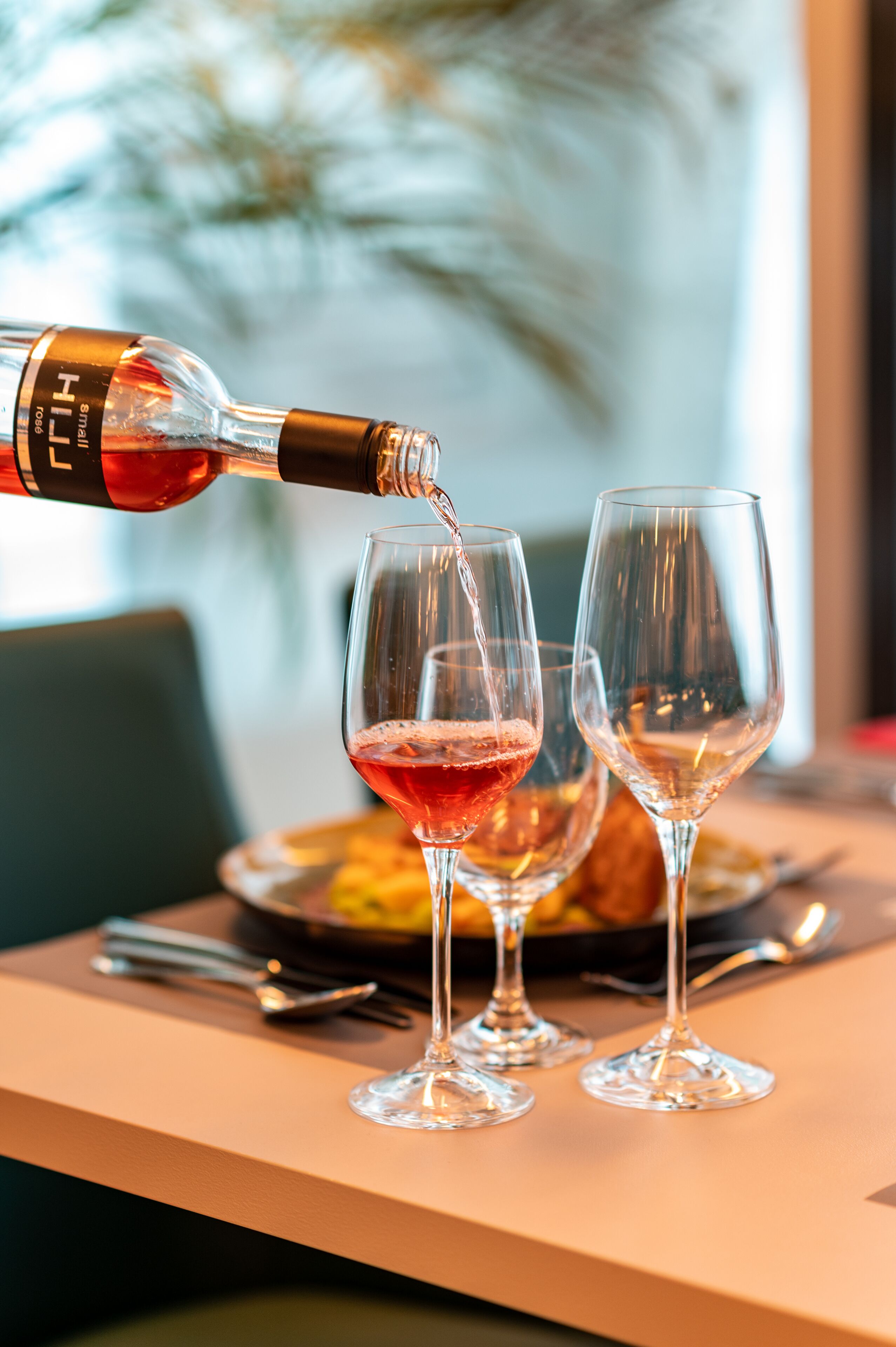 A bottle of wine being poured into two wine glasses on a table.