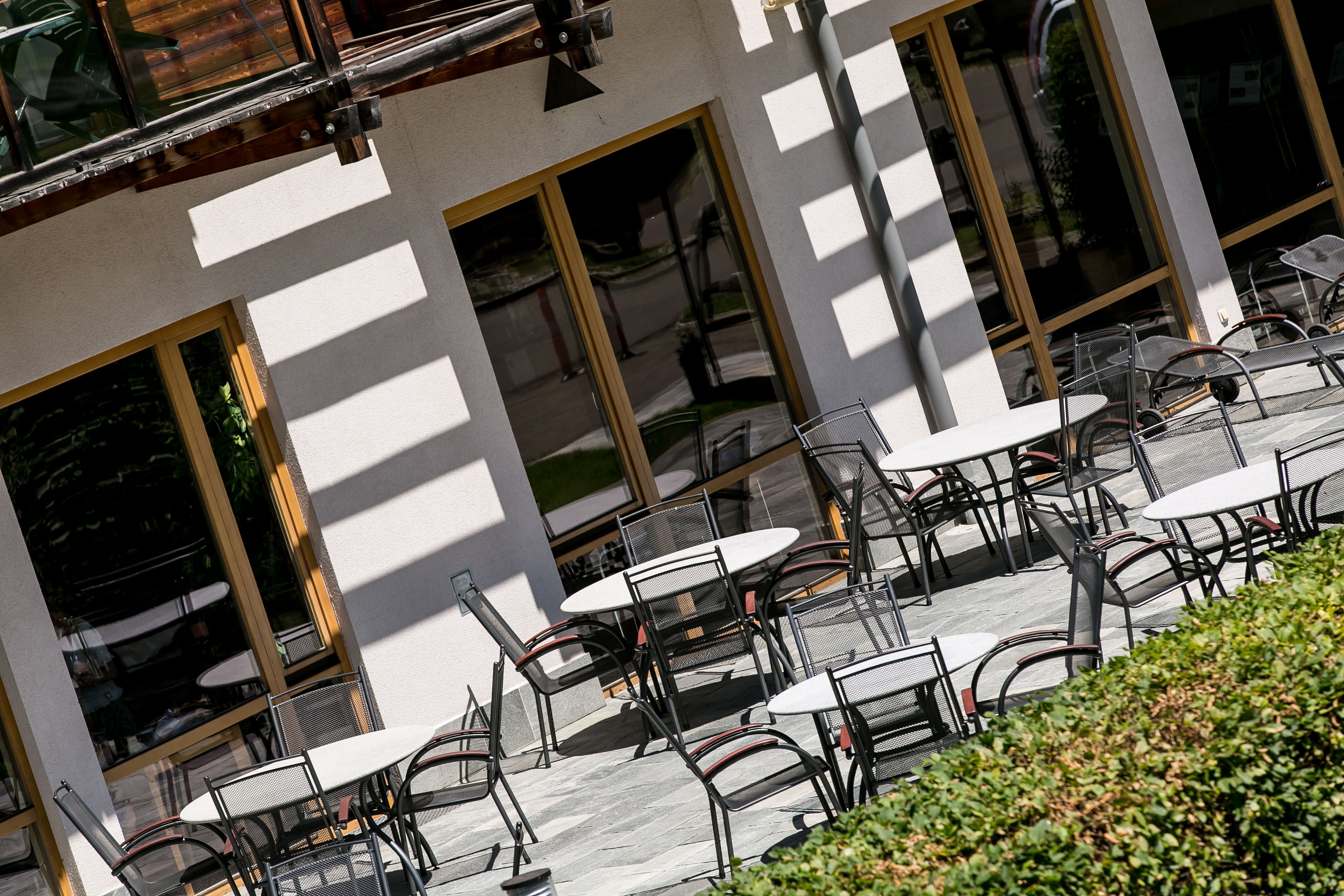 Un espace extérieur aménagé avec des tables et des chaises, de grandes fenêtres et la façade d’un bâtiment.