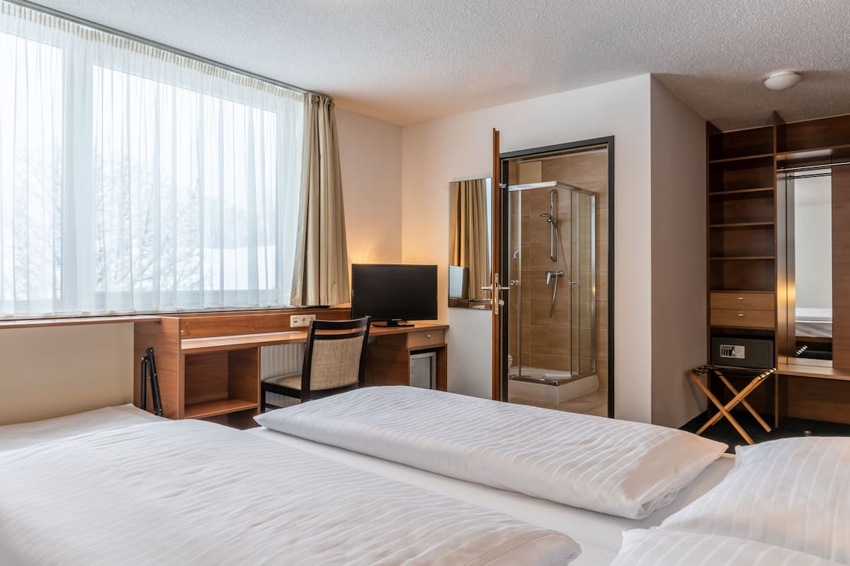 Quarto de hotel com duas camas, uma escrivaninha com cadeira, televisão, chuveiro e guarda-roupa.