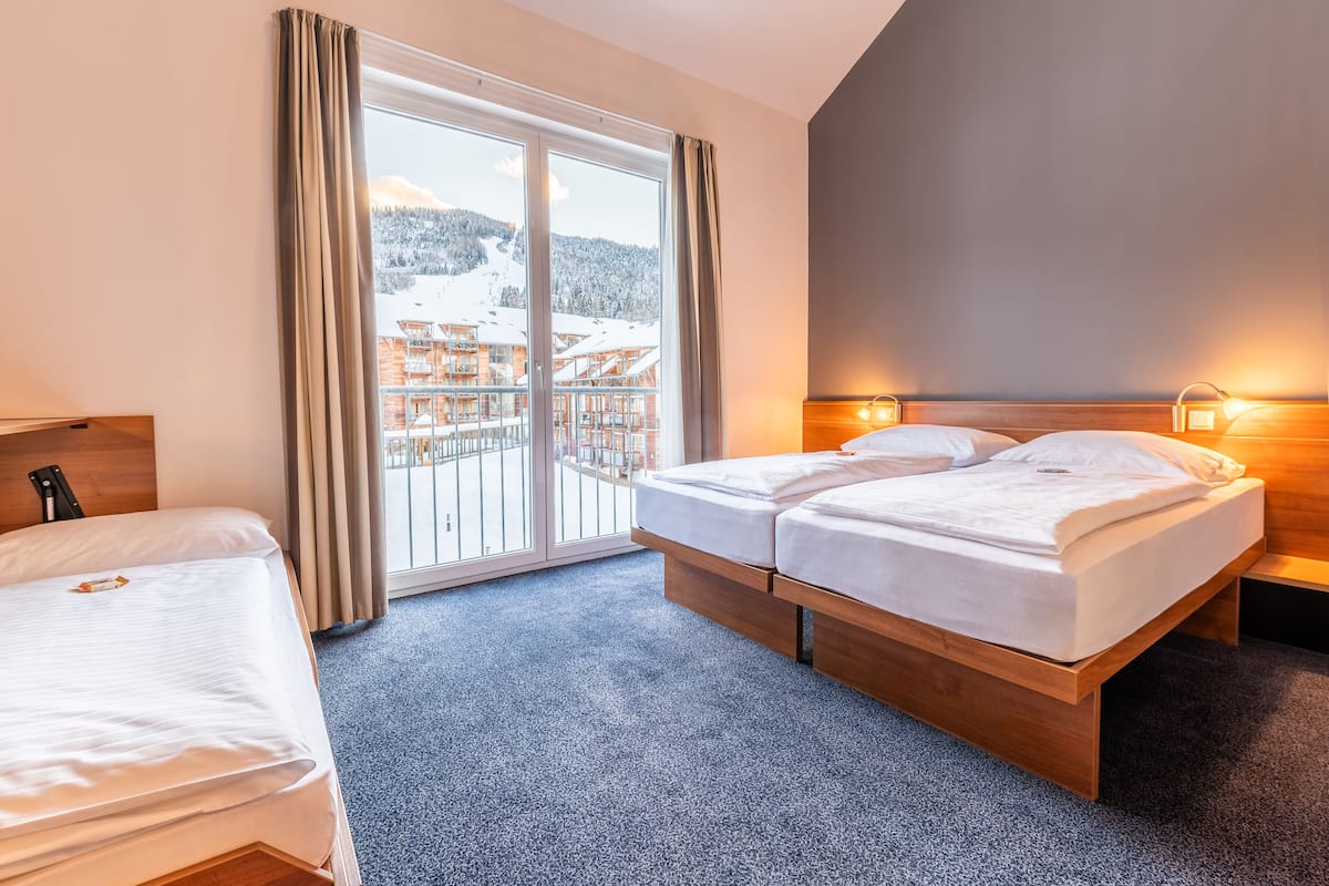 Quarto de hotel com cama, escrivaninha e vista para uma montanha nevada e edifícios.