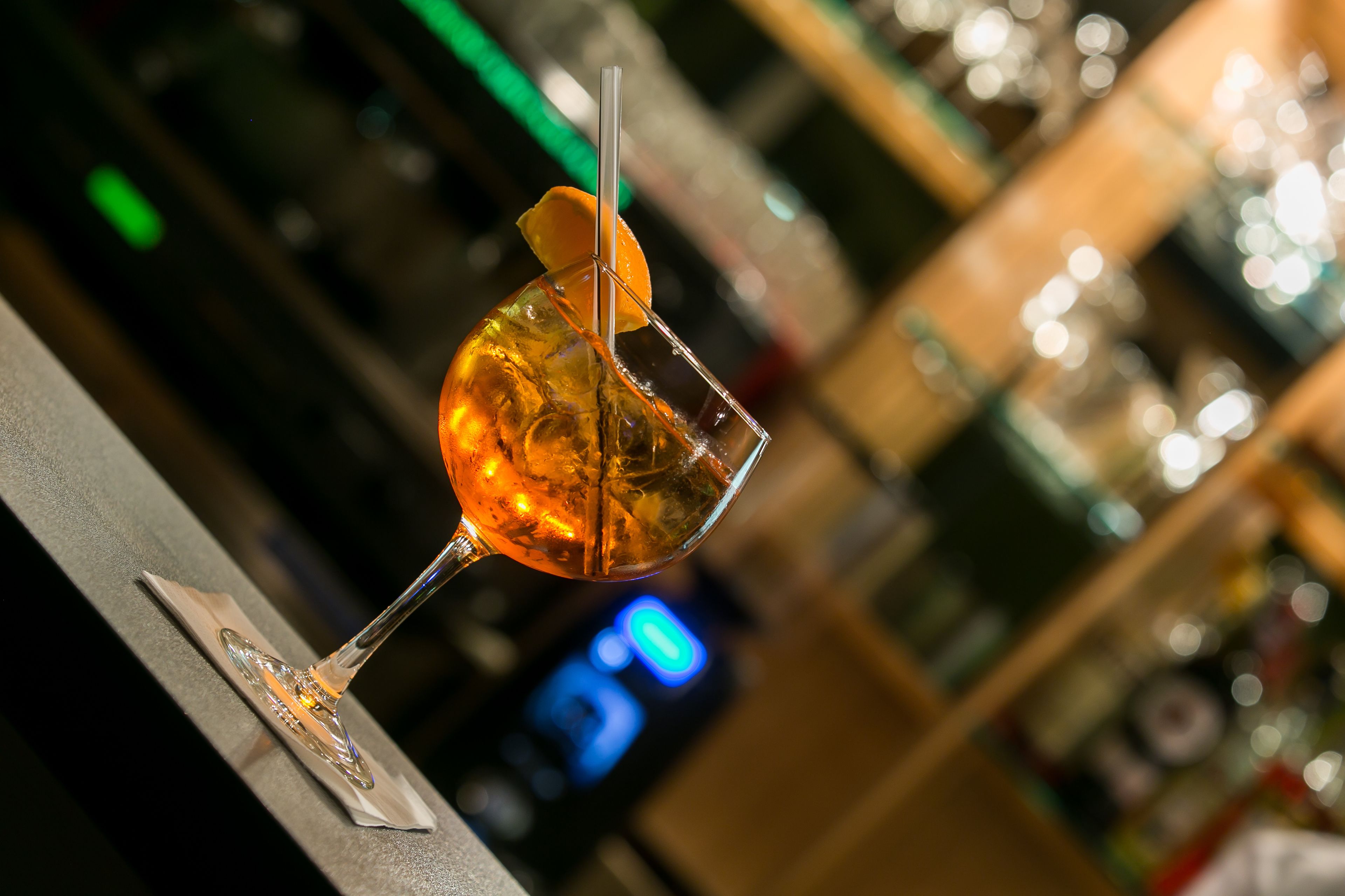 Um copo de cocktail com canudo e uma rodela de laranja em um balcão de bar.