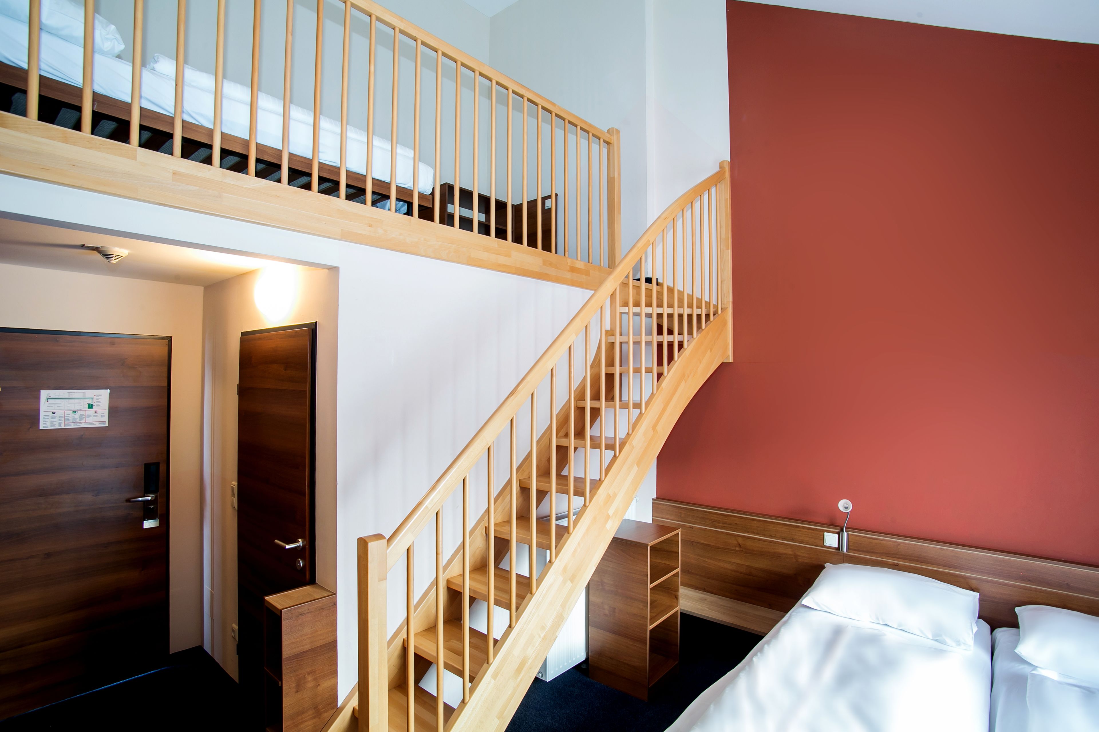 Una habitación de hotel con una escalera de madera, una cama con ropa blanca y una pared de acento roja.