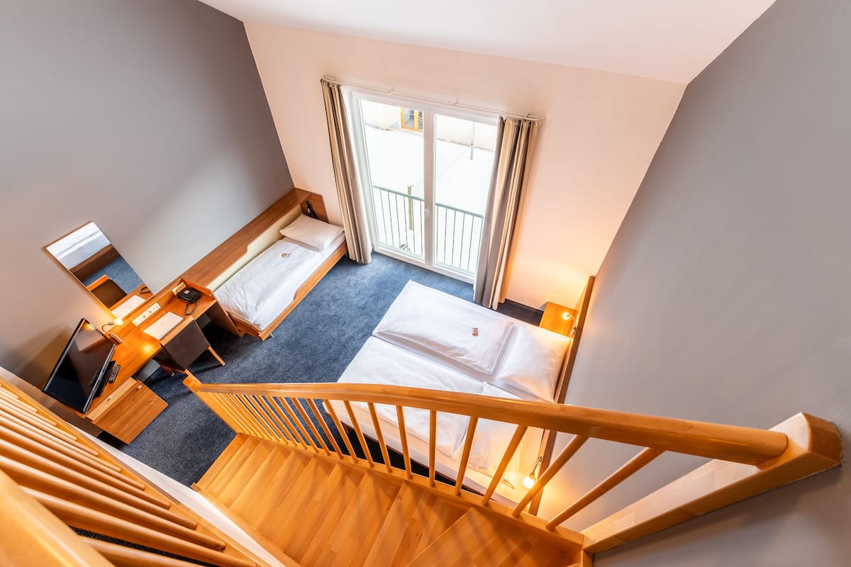 Quarto de hotel com escada de madeira, duas camas, uma escrivaninha com computador e uma janela grande com cortinas.
