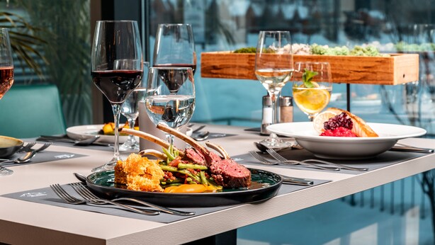 A dining table with a meal, wine glasses, and a view of the outdoors. - Club Hotel am Kreischberg (Sankt Georgen am Kreischberg)