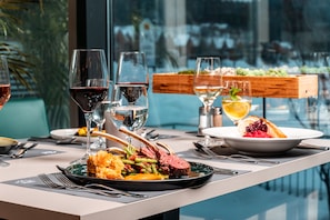 A dining table with a meal, wine glasses, and a view of the outdoors. - Club Hotel am Kreischberg (Sankt Georgen am Kreischberg)