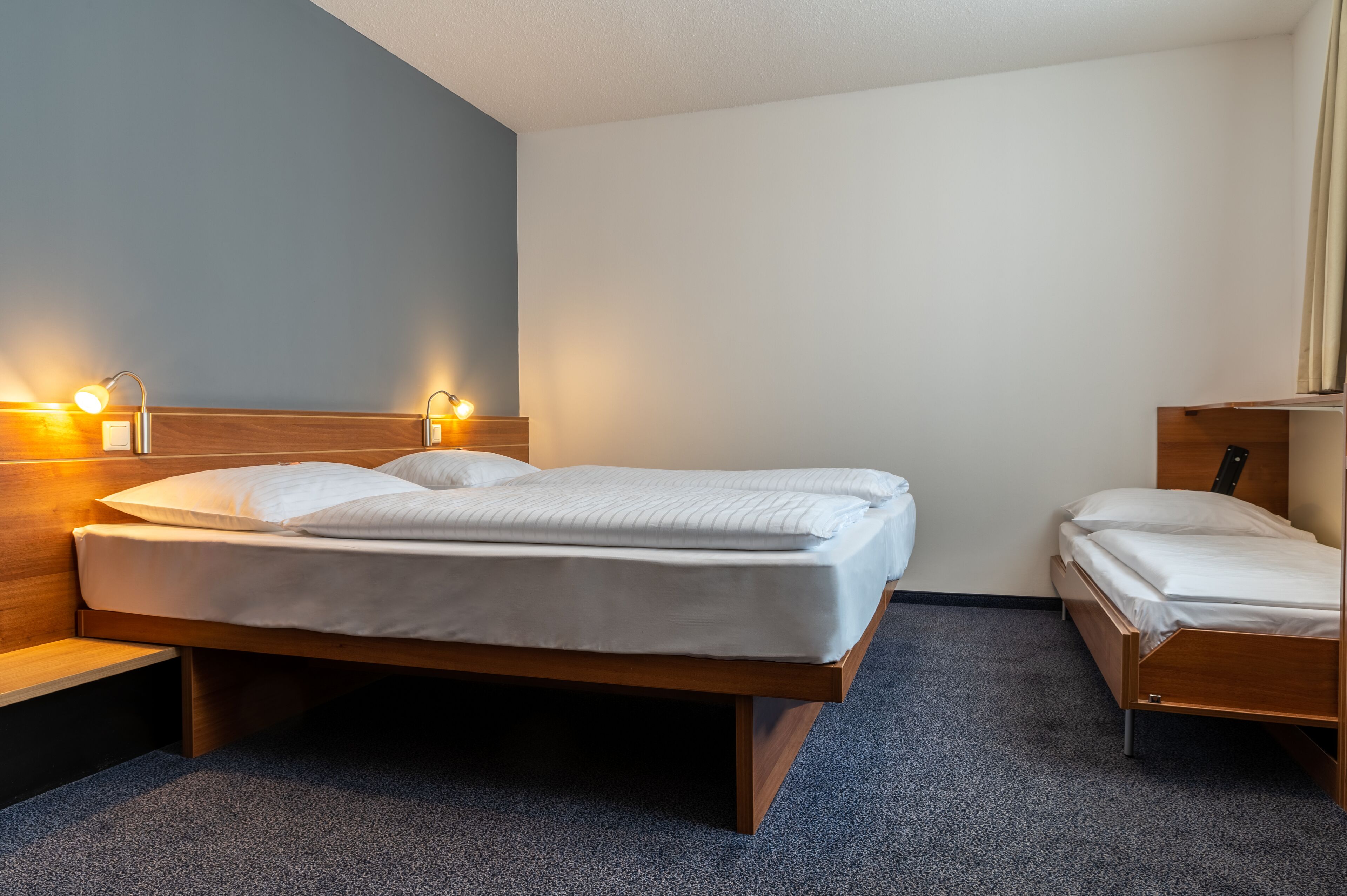 Ein Einzelbett mit Holzrahmen und Kopfteil, ein Nachttisch und zwei an der Wand befestigte Leselampen.