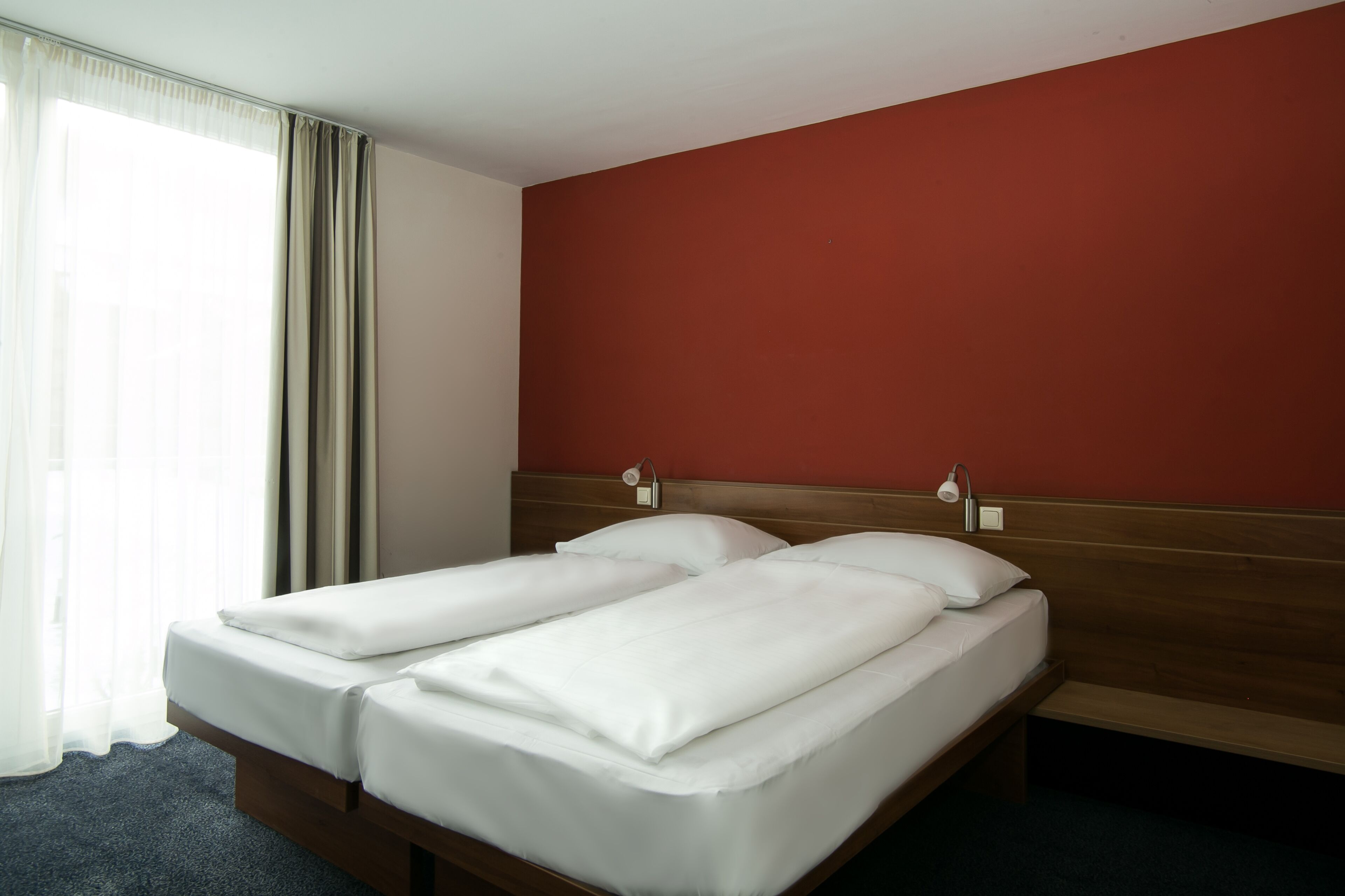 Une chambre d’hôtel avec un lit double, une tête de lit en bois, une table de chevet et une fenêtre avec des rideaux.