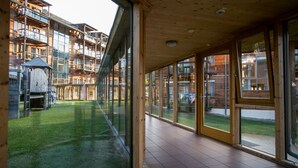 A spacious indoor area with large windows, a tiled floor, and a view of a wooden building with multiple balconies. - Club Hotel am Kreischberg (Sankt Georgen am Kreischberg)