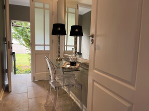 A glass-top table with two lamps and a decorative item, a clear chair, and a door leading to a garden. - Patcham Place B&B (Clarens)