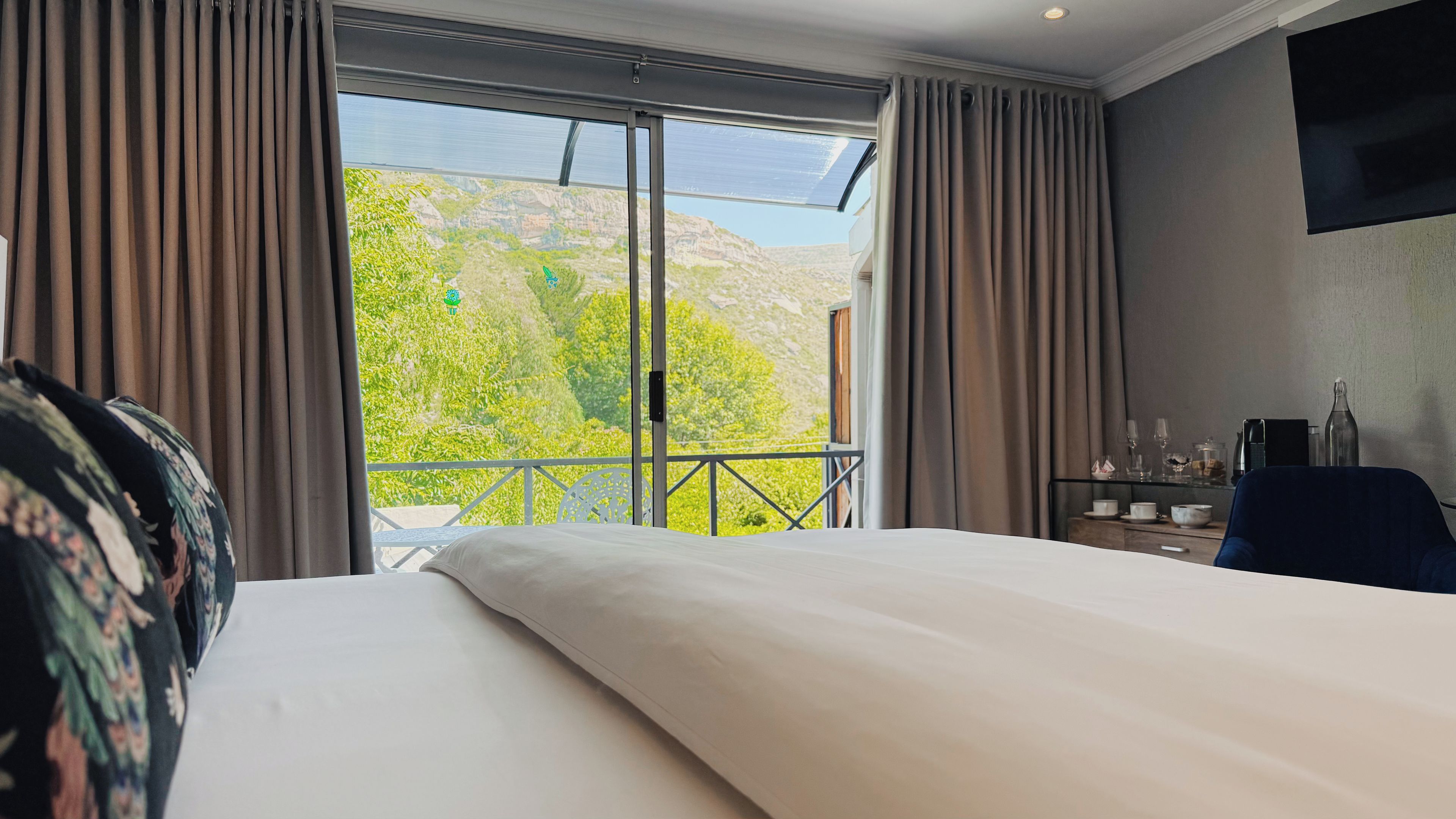 A hotel room with a large bed, a balcony with a mountain view, and a desk with a chair.