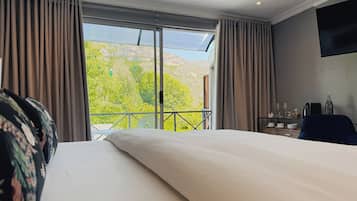Une chambre d’hôtel avec un grand lit, un balcon offrant une vue sur la montagne et un bureau avec une chaise.