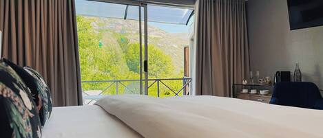 A hotel room with a large bed, a balcony with a mountain view, and a desk with a chair.
