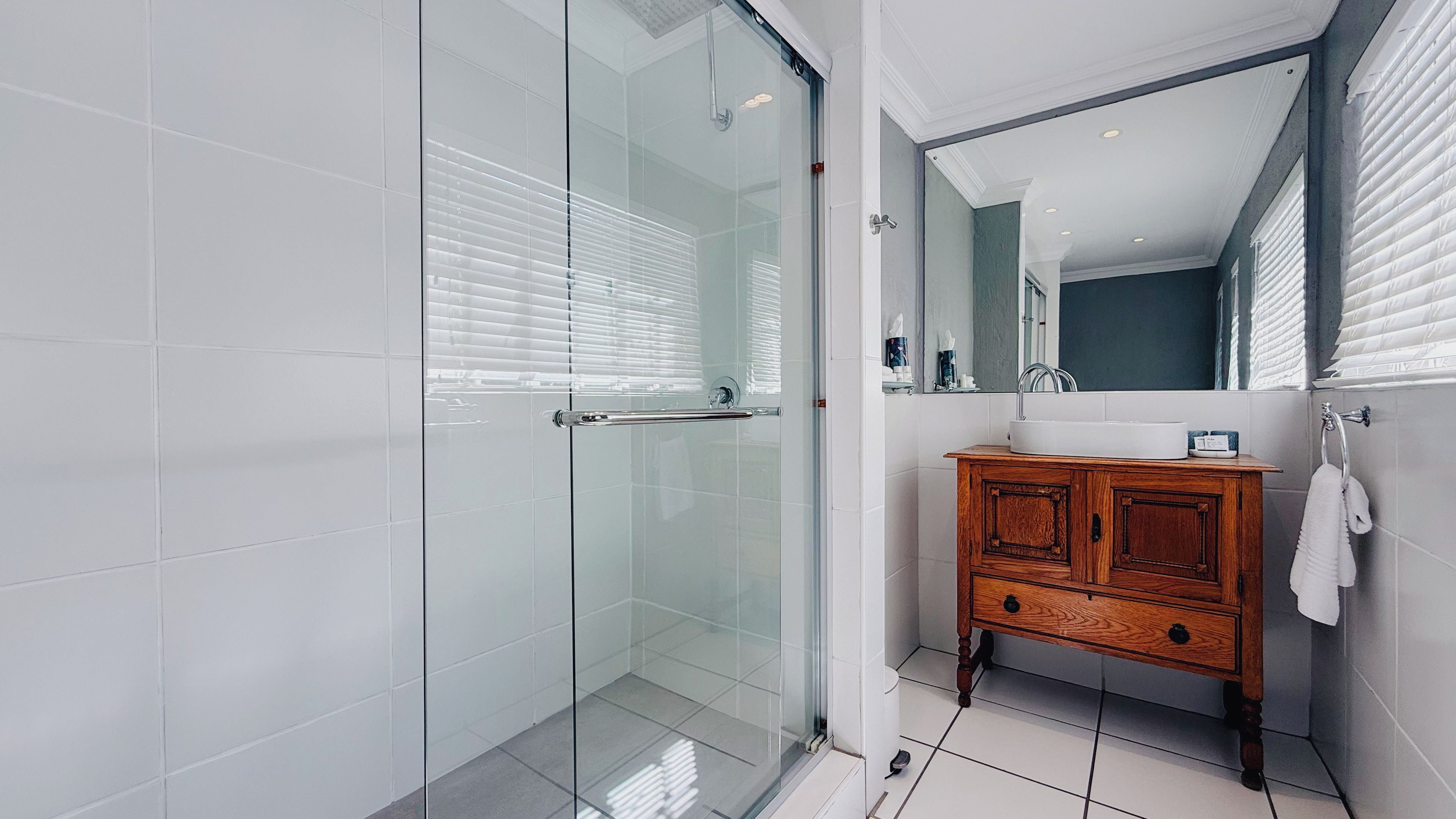 A modern bathroom with a glass shower enclosure, a wooden vanity with a mirror, and a white towel hanging on the wall.