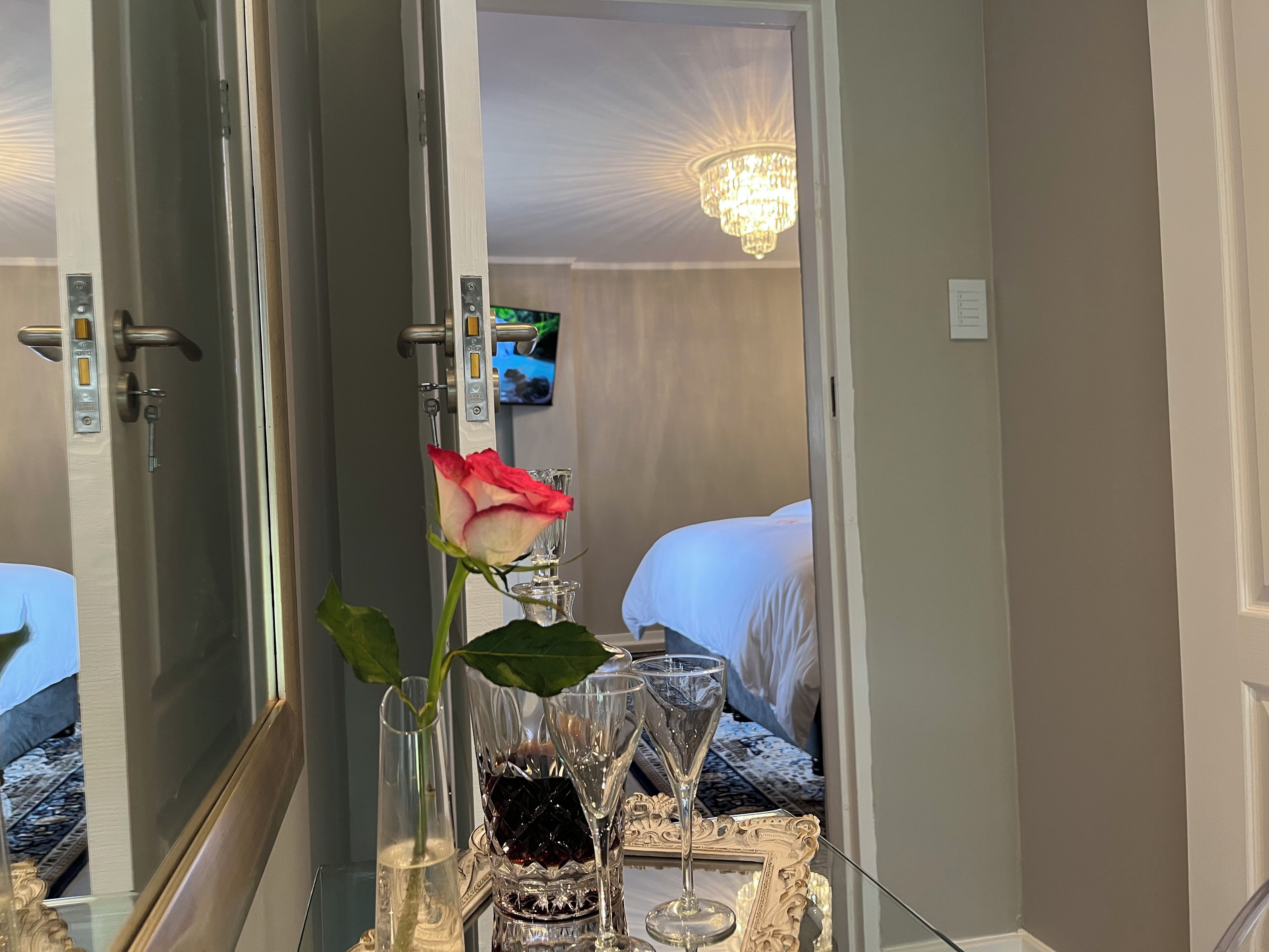 A hotel room with a bed, a television, a chandelier, and a table with a vase of flowers and glasses.