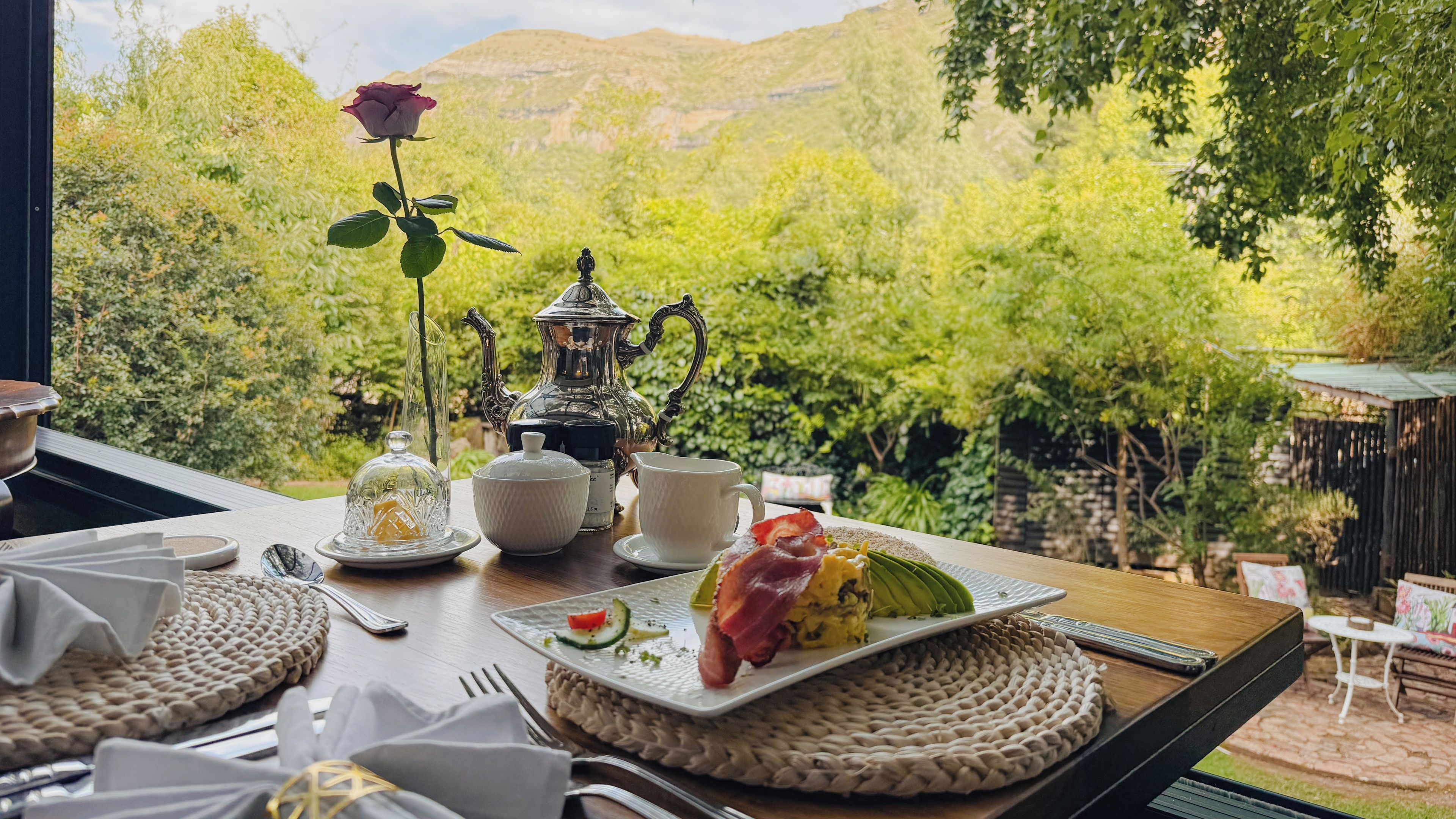 Une table à manger dressée avec une assiette de nourriture, une théière, des tasses et une rose.