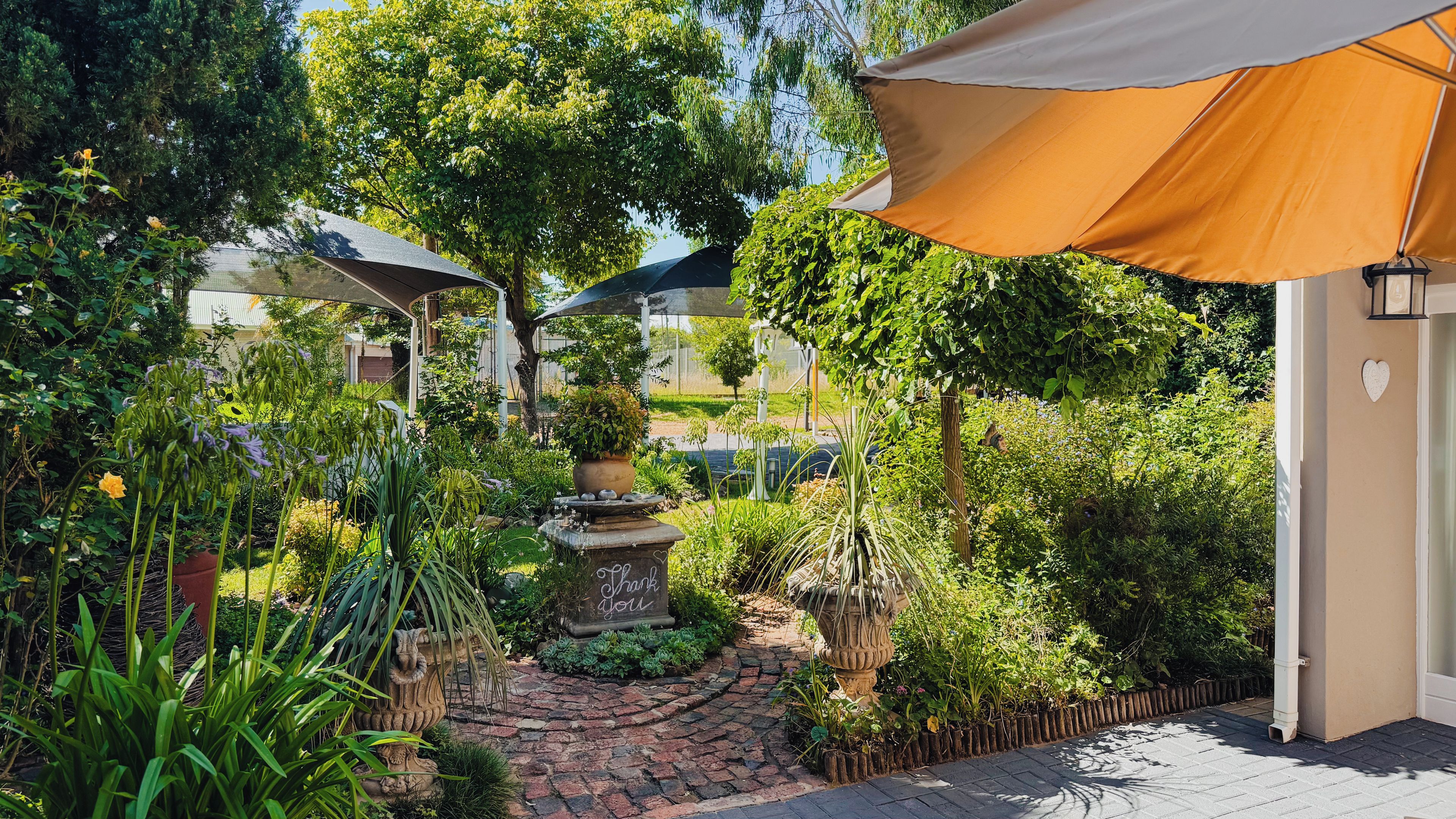 Un jardin agrémenté d’une fontaine en pierre, de plantes en pot et d’un chemin bordé de briques.