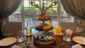 Une table à manger agrémentée d’un plateau à trois niveaux présentant des fruits et des fromages, de bougies et une bouteille de miel.