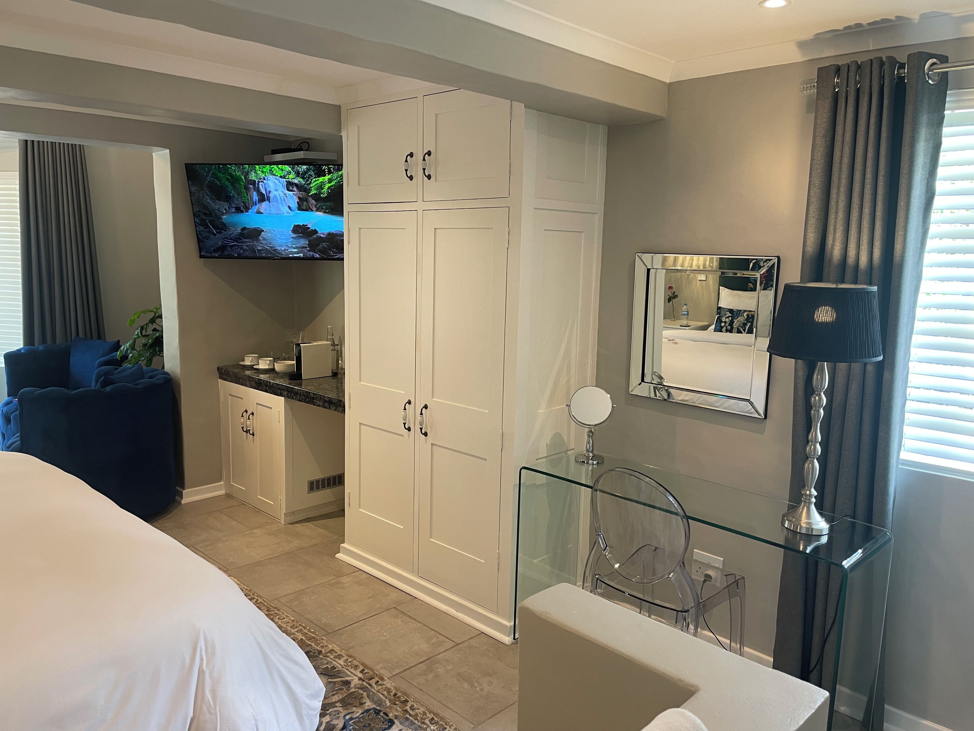 A bedroom with a bed, a TV, a wardrobe, a bathroom with a mirror, and a glass table.