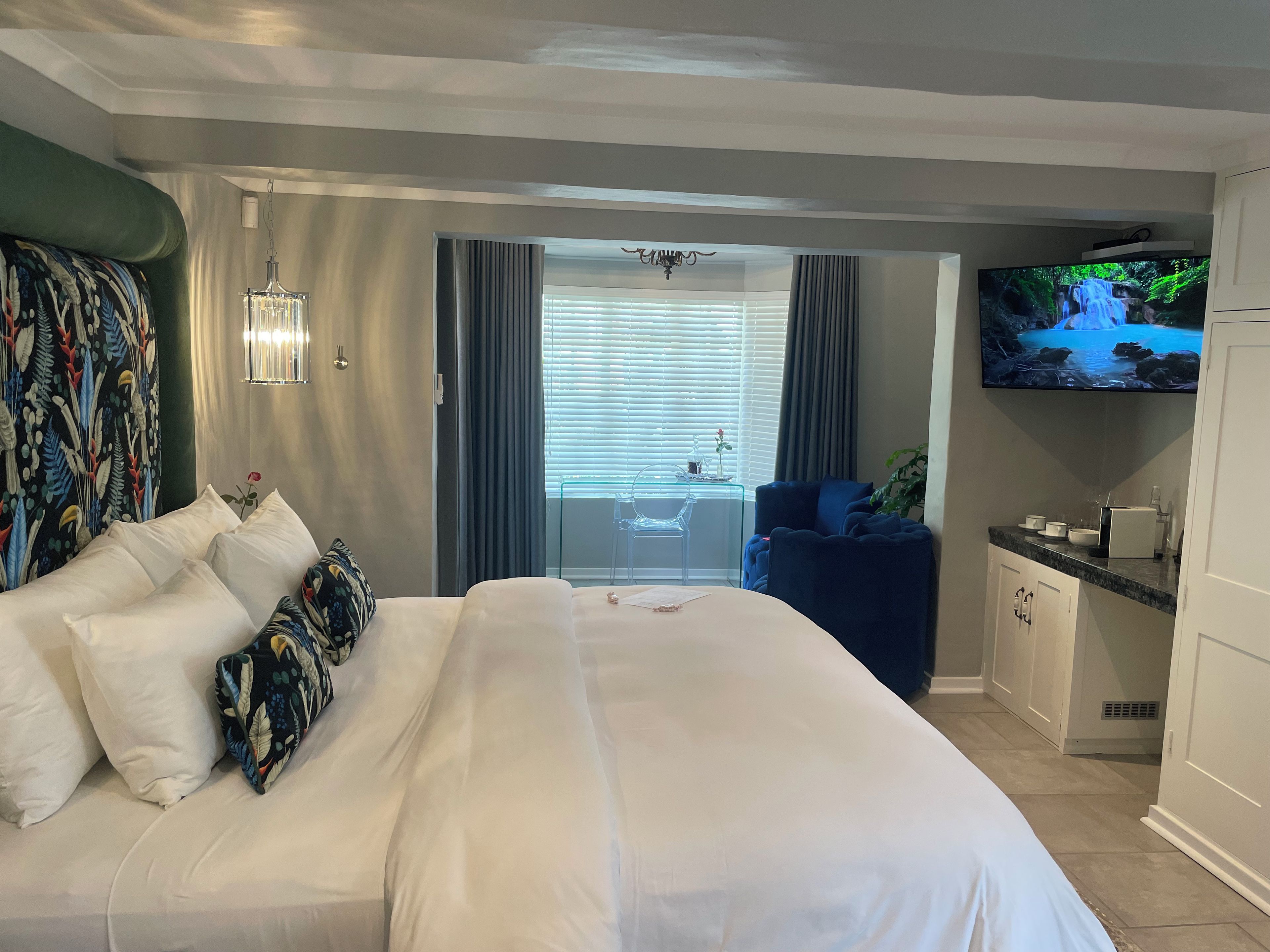 A hotel room with a large bed, a TV on the wall, a desk with a sink, and a view of the outdoors through the window.