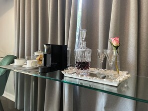 A hotel room with a glass table set for breakfast, including a coffee maker, a crystal decanter, and a vase with a rose. - Patcham Place B&B (Clarens)
